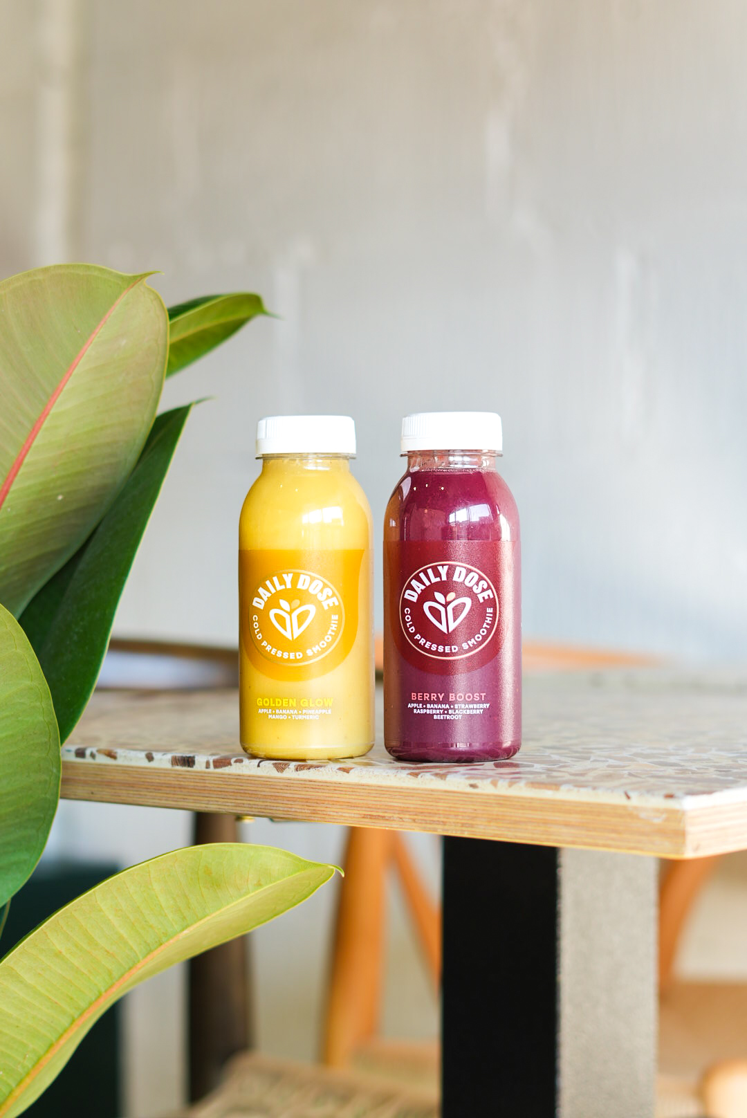 Two Daily Dose cold-pressed smoothies on a terrazzo shelf