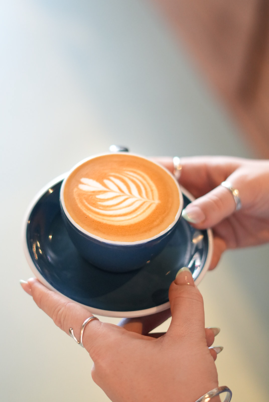 Hands holding a navy cup and saucer with a rosetta latte art flat white