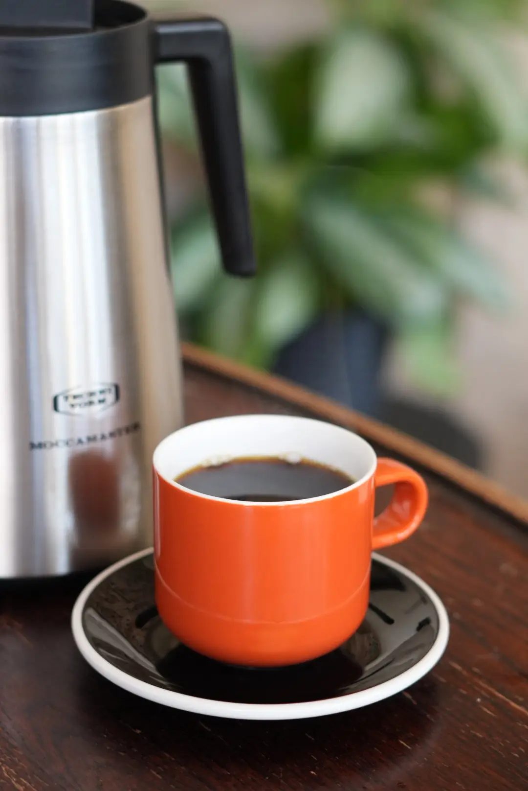 Orange cup of batch brew next to a Moccamaster