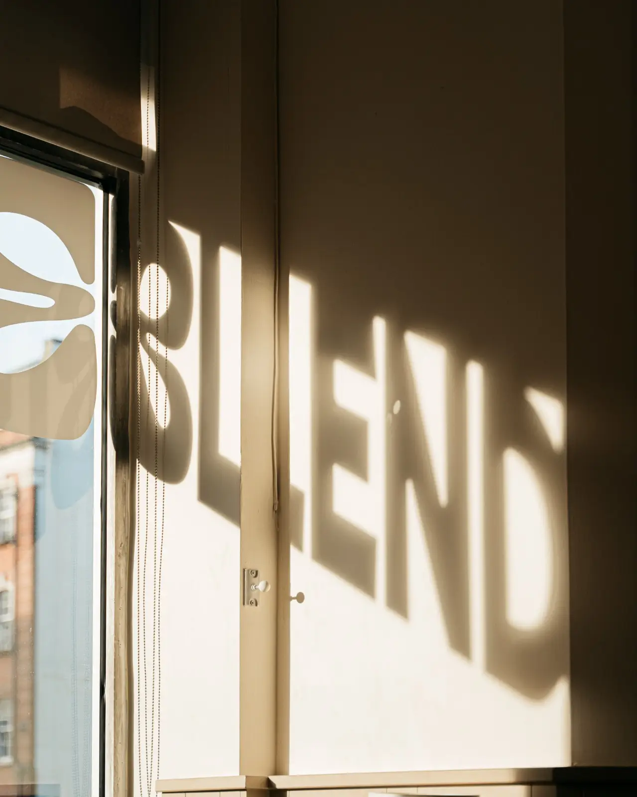 Sunlight casting the BLEND window decal across a quiet café wall